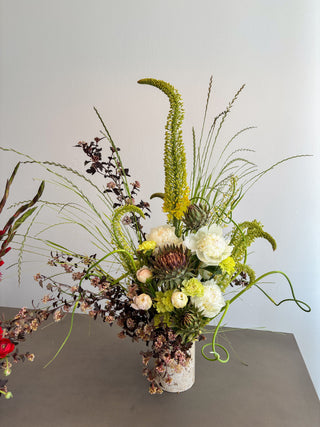 Floral arrangement with greenery and white flowers in a ceramic vase on a gray surface.