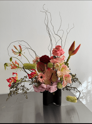 Floral arrangement in a black vase on a reflective surface with a white background