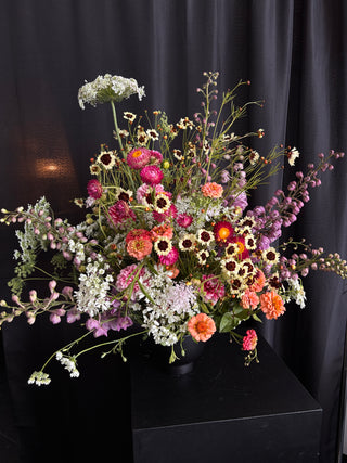 Colorful flower arrangement on a black pedestal against a dark curtain background