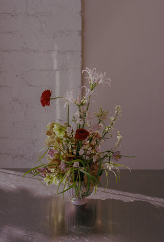 Floral arrangement in a vase on a reflective surface with a textured wall background