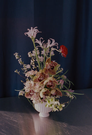 Floral arrangement in a white vase on a reflective surface with a dark background