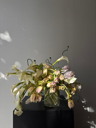 Bouquet of flowers in a clear vase on a reflective surface with a dark background