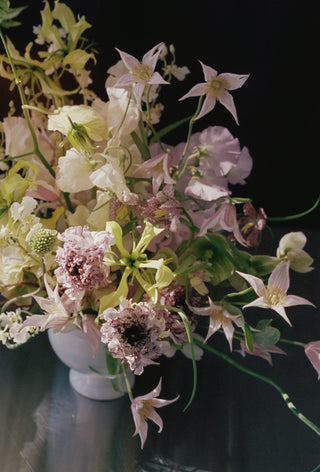 Bouquet of flowers in a white vase on a reflective surface with a dark background