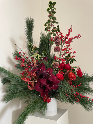 Decorative floral arrangement with red flowers and greenery on a white surface
