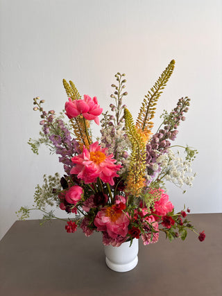 Bouquet of pink and wild flowers in a white vase against a neutral background