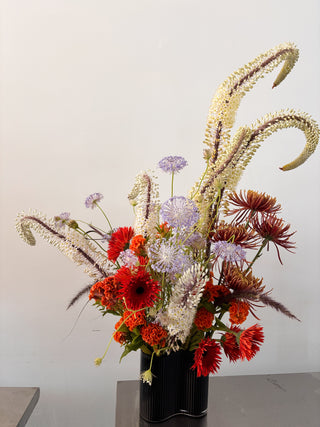 Floral arrangement with red, purple, and white flowers in a black vase on a gray surface.