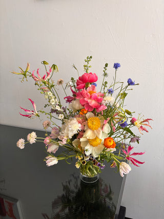 Bouquet of colorful peonies and wildflowers in a clear vase against a plain background