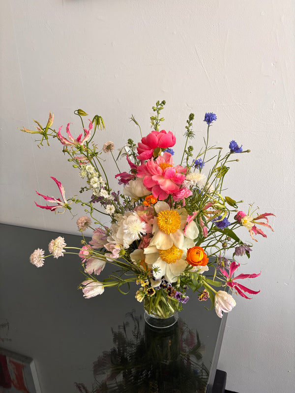 Bouquet of colorful peonies and wildflowers in a clear vase against a plain background