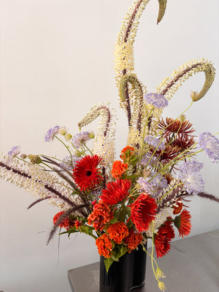 Floral arrangement with red and orange flowers in a black vase on a light background