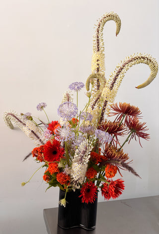 Floral arrangement with red, white, and purple flowers in a black vase on a light background